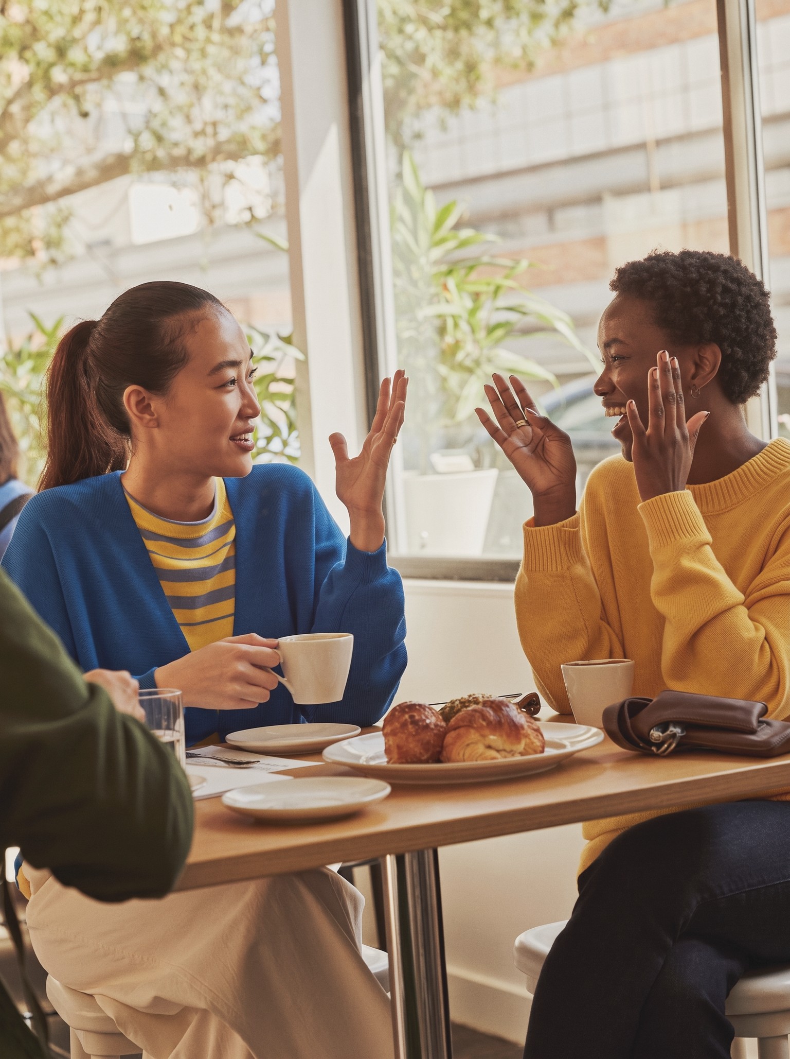 Two friends talking and laughing at a caf&eacute; table.